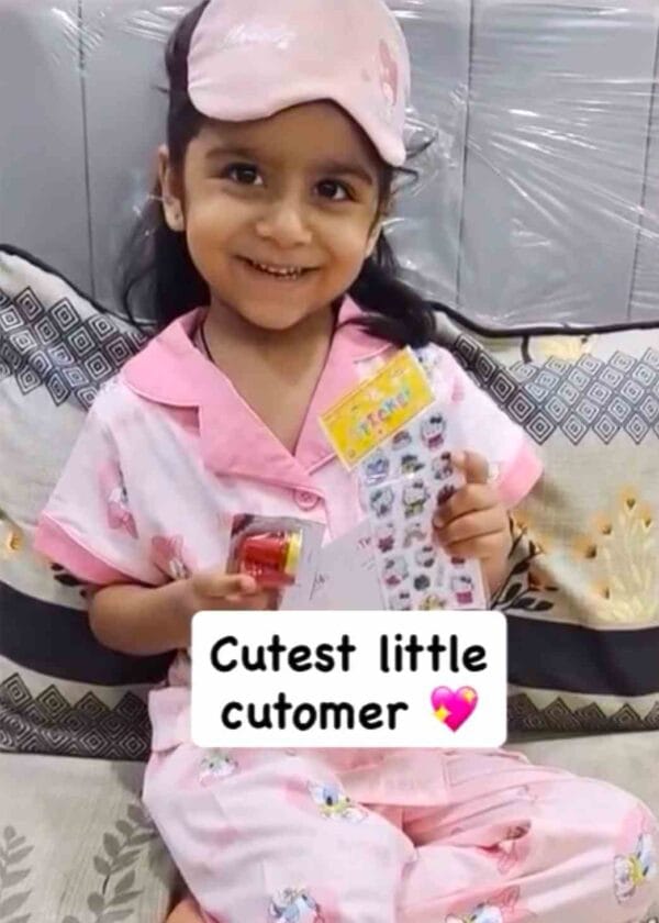 Photo of a smiling girl in pink Kuku Kids nightwear holding the free sticker pack that came with her parcel